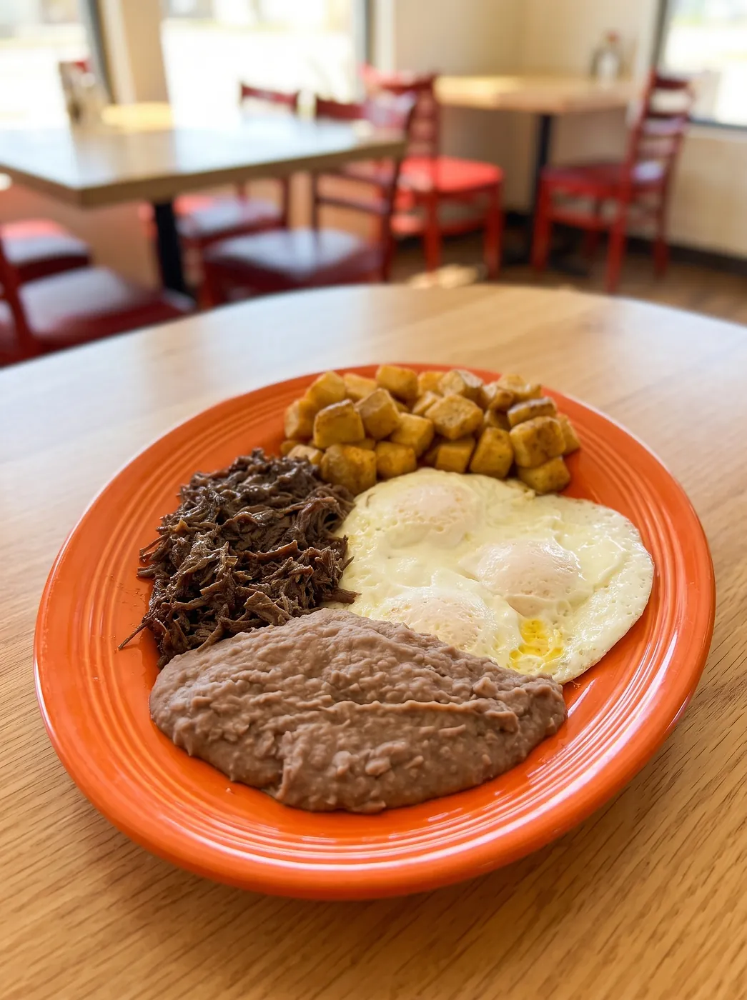 Barbacoa plate with two eggs, breakfast potatoes and refried beans on an orange platter