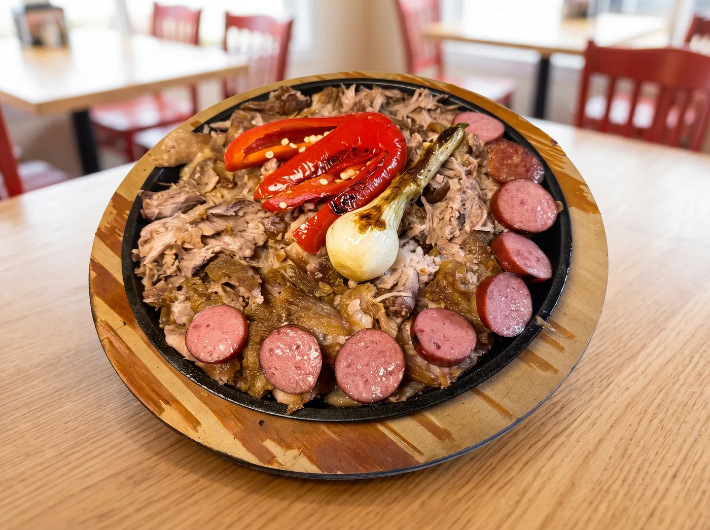 Sizzling skillet of slow-cooked pork ringed with sliced sausage, served on a wooden board