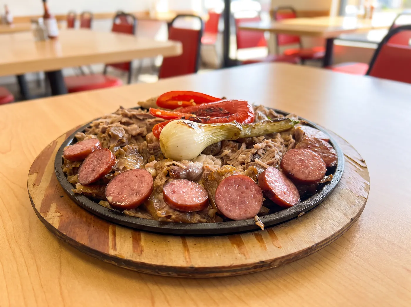 Cast-iron skillet of slow-cooked pork with sliced sausage, roasted red pepper and a grilled spring onion